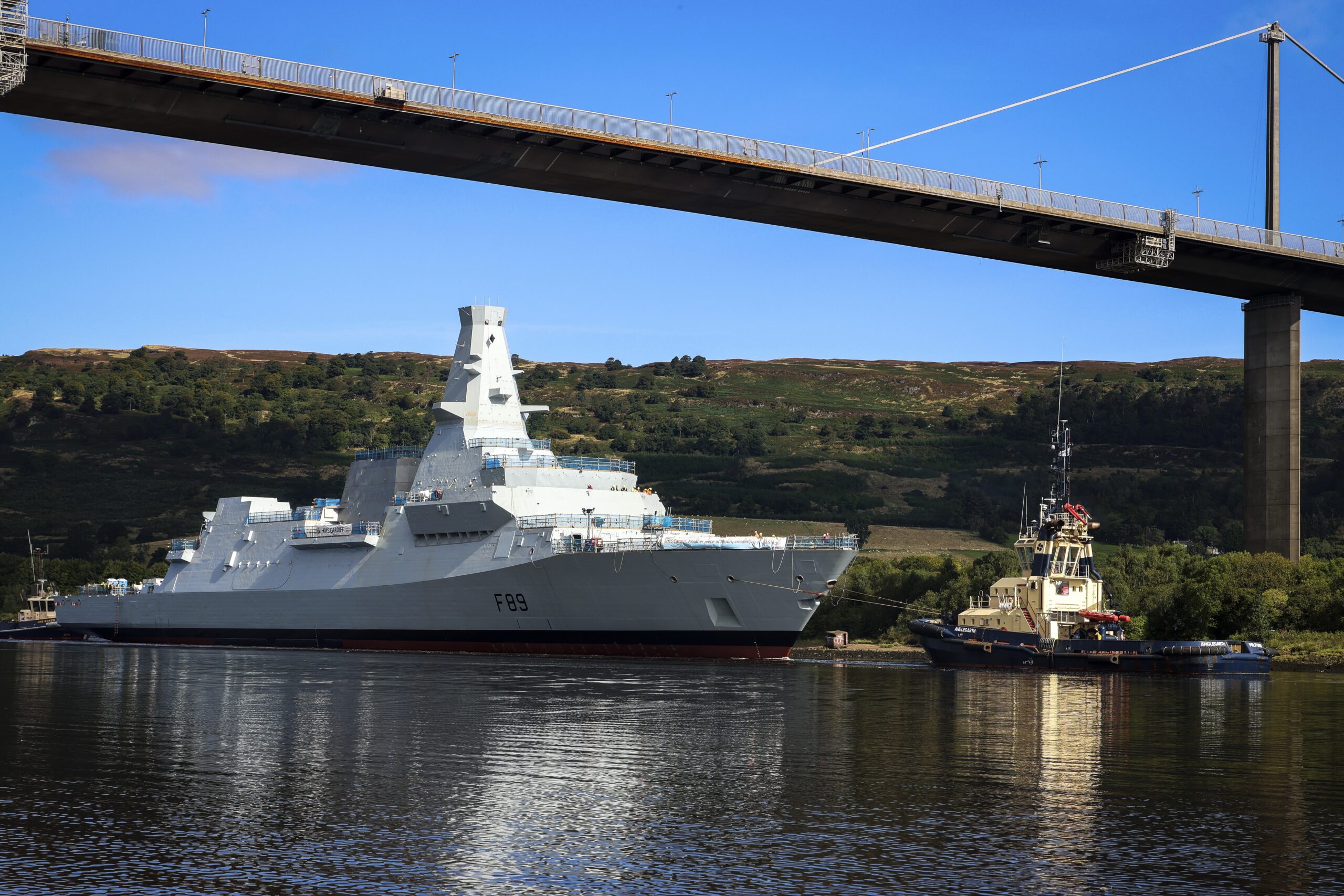 Pictured: Type 26 Frigate HMS Cardiff being towed and maneuvered as she passes under the Erskine Bridge on the Clyde.HMS Cardiff, the second of the Royal Navys new City Class Type 26 frigates, was loaded onto a giant barge last week. The ship, which weighs almost 7,000 tonnes, sailed down the River Clyde on Friday, August 30 to Loch Long, where she was lowered into the water for the first time at Glen Mallan. HMS Cardiff then made her way back up the Clyde to BAE Systems yard at Scotstoun where the work to fit the warship out will be completed. Currently Scottish shipyards have orders to build 13 Royal Navy frigates, with the Type 31 vessels being built by Babcock at Rosyth on the east coast, and the Type 26 ships being constructed by BAE Systems on the Clyde.
